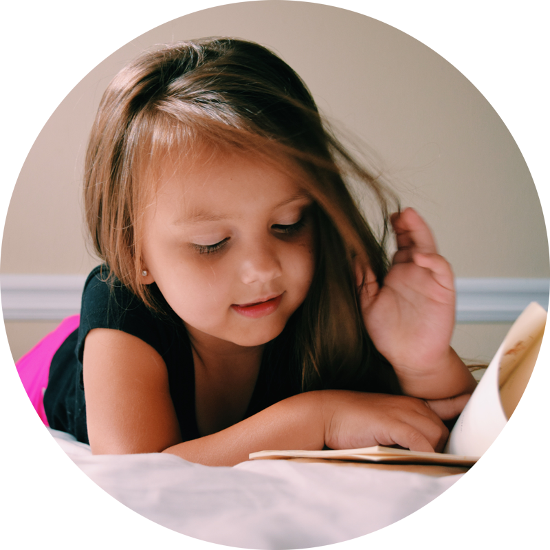 cute little girl reading a book on her bed