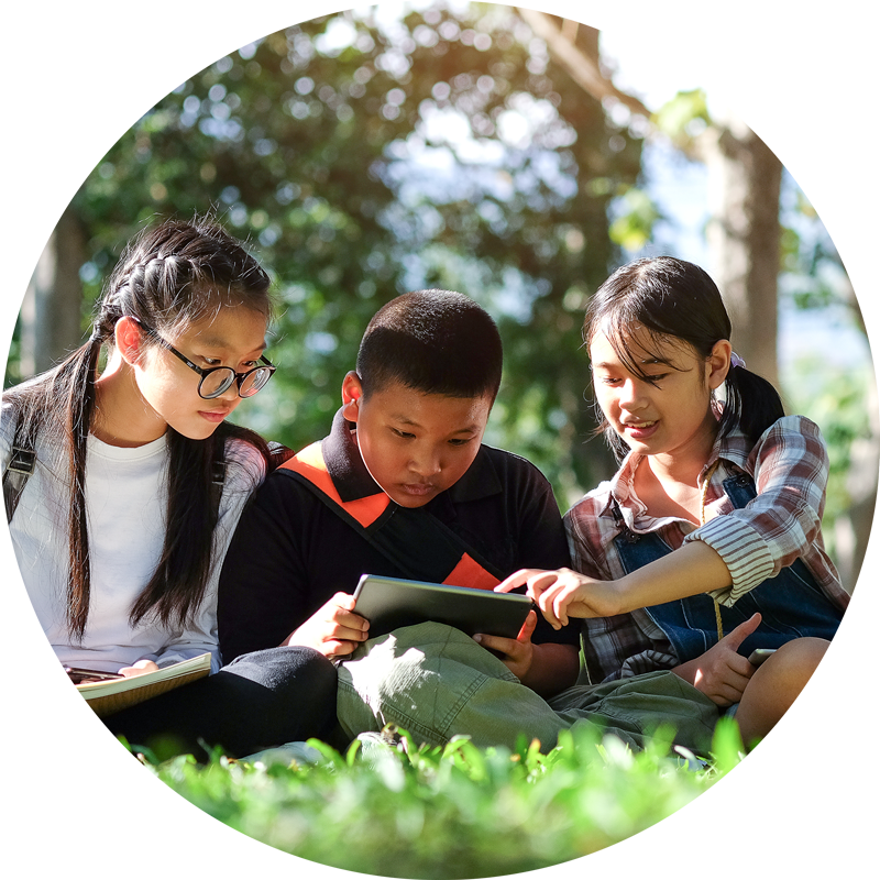 Two Asian girls and one Asian boy reading in the grass together